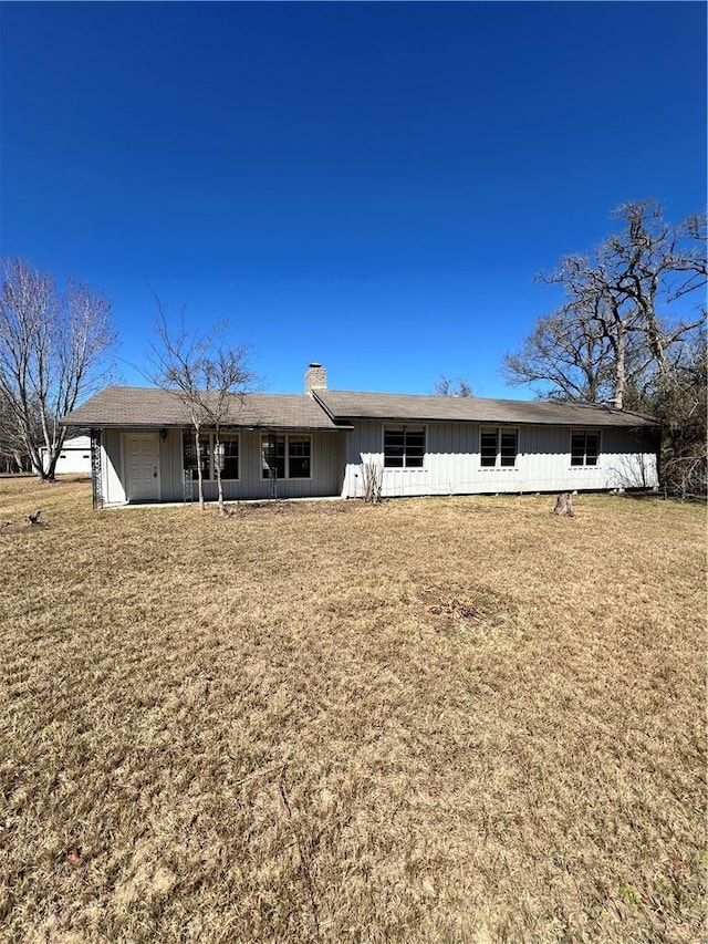 back of house featuring an attached garage, a chimney, and a lawn