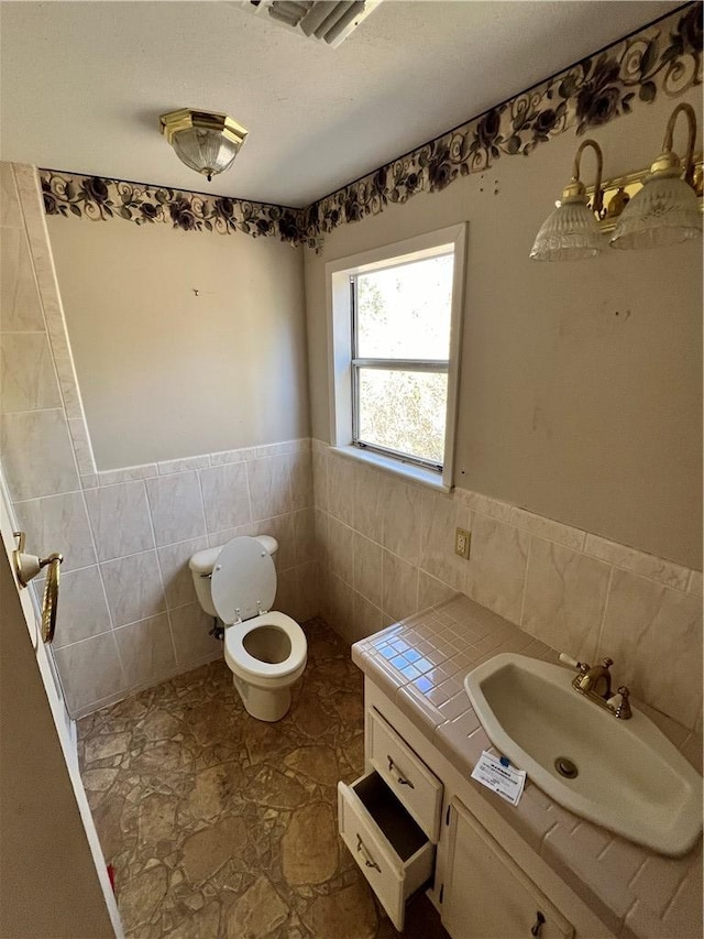 bathroom with vanity, visible vents, a wainscoted wall, tile walls, and toilet