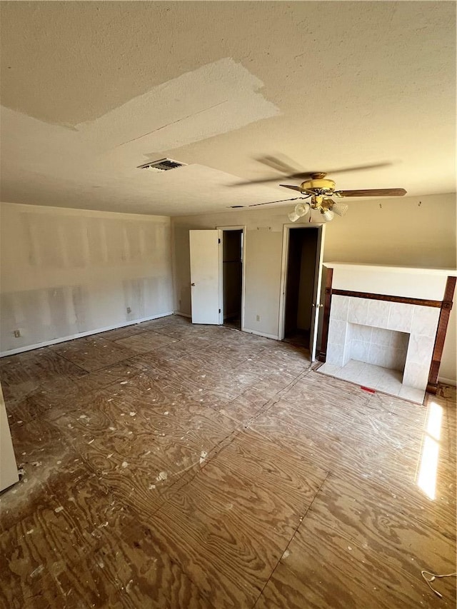 unfurnished living room with visible vents, a fireplace, a textured ceiling, and ceiling fan