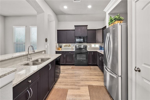 kitchen with light stone counters, dark brown cabinetry, sink, black appliances, and light hardwood / wood-style floors