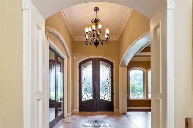 entryway with french doors, ornamental molding, and an inviting chandelier