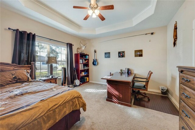 carpeted bedroom featuring a tray ceiling, crown molding, baseboards, and ceiling fan
