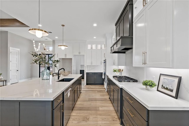 kitchen with sink, appliances with stainless steel finishes, white cabinets, decorative light fixtures, and a large island with sink