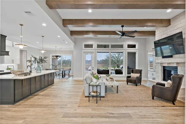 living room with beamed ceiling, a stone fireplace, ceiling fan, and light hardwood / wood-style flooring