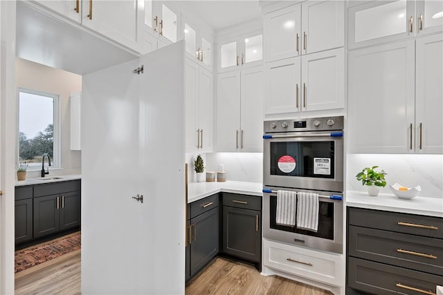 kitchen with sink, backsplash, white cabinets, light hardwood / wood-style floors, and stainless steel double oven