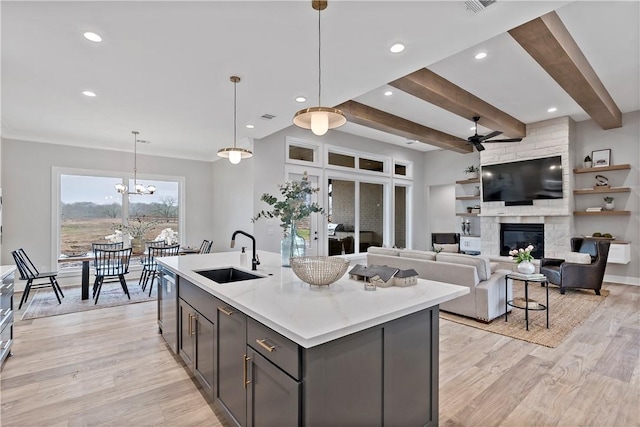 kitchen featuring sink, decorative light fixtures, a center island with sink, light wood-type flooring, and a fireplace