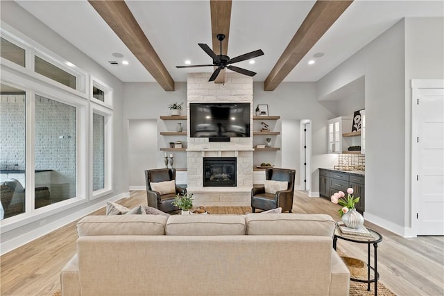 living room with beamed ceiling, ceiling fan, a fireplace, and light hardwood / wood-style flooring