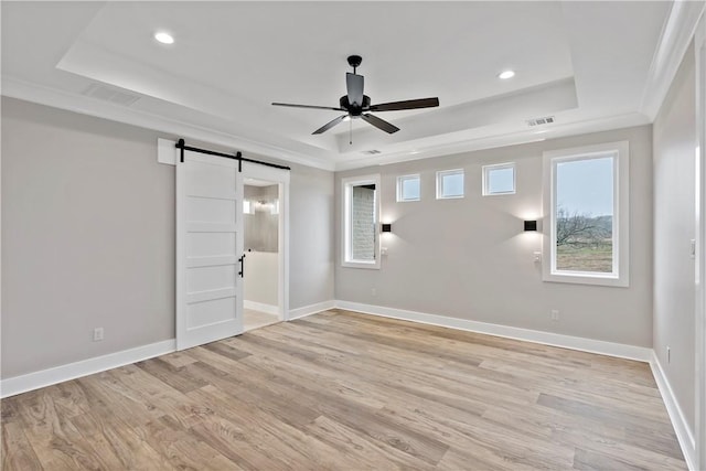 spare room featuring a barn door, a raised ceiling, and light hardwood / wood-style floors