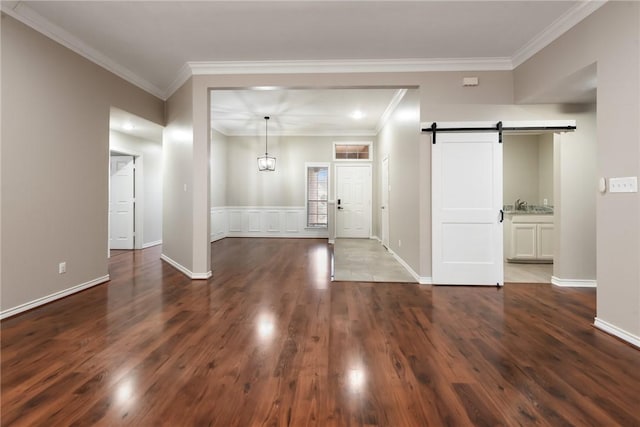 foyer entrance with ornamental molding, a barn door, dark wood-type flooring, and baseboards