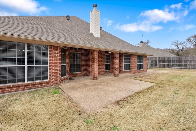 back of house with a patio, a chimney, roof with shingles, fence, and brick siding