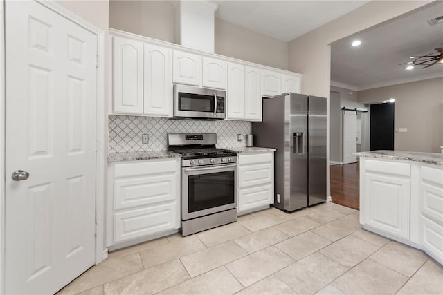 kitchen featuring ceiling fan, a barn door, white cabinetry, appliances with stainless steel finishes, and backsplash