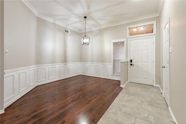 entryway with crown molding, visible vents, an inviting chandelier, wainscoting, and wood finished floors