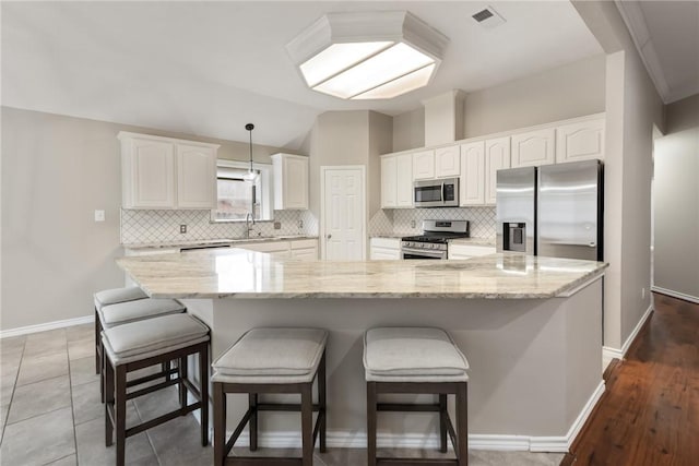 kitchen featuring light stone counters, stainless steel appliances, visible vents, white cabinets, and a sink