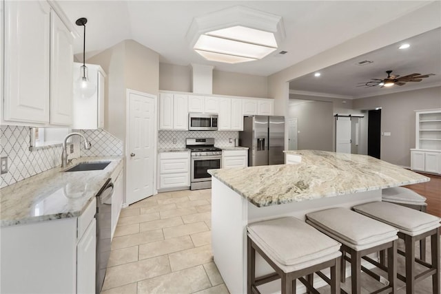 kitchen featuring a barn door, appliances with stainless steel finishes, a ceiling fan, a kitchen island, and a sink