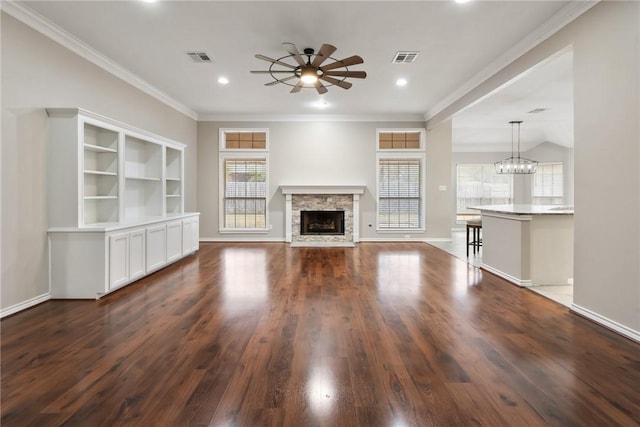 unfurnished living room with ceiling fan with notable chandelier, dark wood-type flooring, a fireplace, baseboards, and ornamental molding