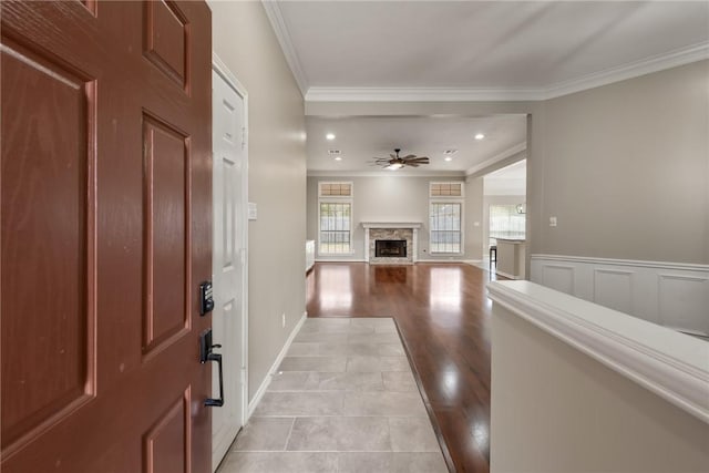 foyer entrance with ornamental molding, a wainscoted wall, a fireplace, and a ceiling fan