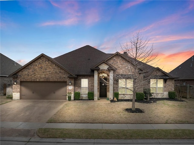 french country inspired facade with a shingled roof, brick siding, driveway, and an attached garage