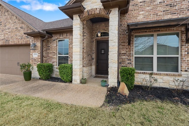 view of exterior entry with a shingled roof, stone siding, brick siding, and an attached garage