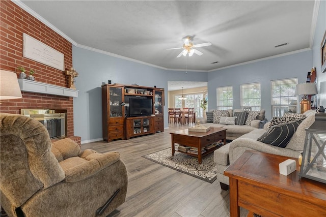 living room with a brick fireplace, ornamental molding, brick wall, ceiling fan with notable chandelier, and light hardwood / wood-style floors