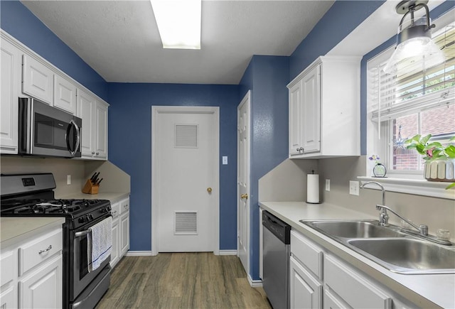 kitchen with appliances with stainless steel finishes, white cabinetry, dark wood-type flooring, and sink