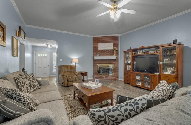 living room with a brick fireplace, crown molding, ceiling fan, and light wood-type flooring