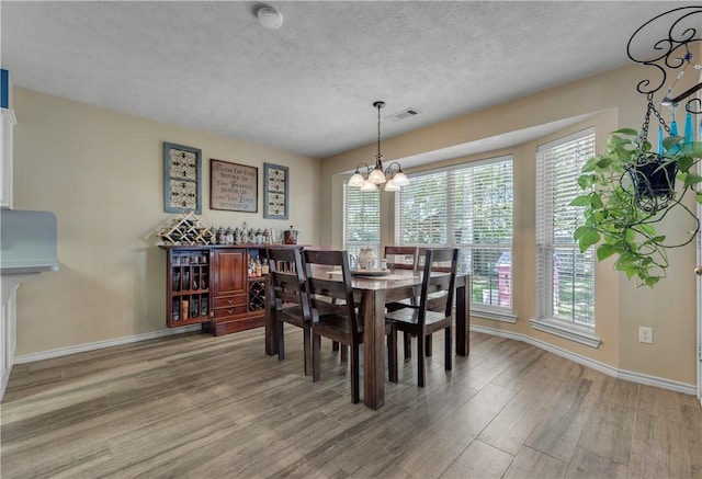 dining space featuring wood-type flooring, a textured ceiling, and a notable chandelier