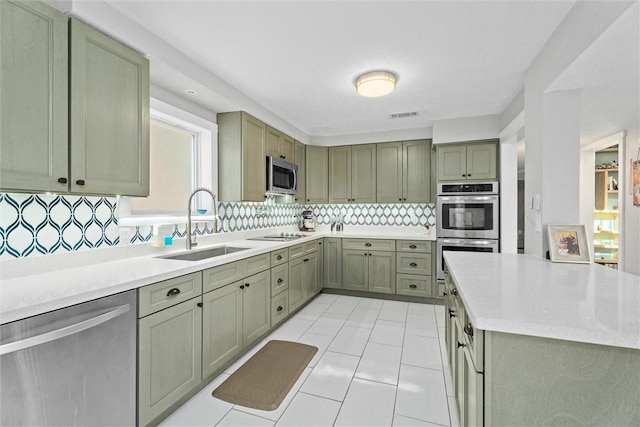 kitchen featuring sink, light tile patterned floors, stainless steel appliances, tasteful backsplash, and green cabinetry