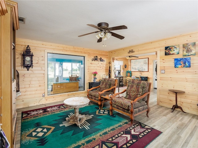 sitting room featuring ceiling fan, wood walls, and light hardwood / wood-style flooring