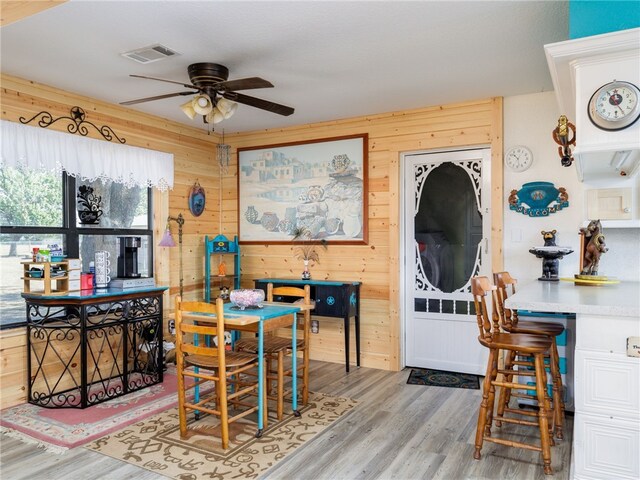 dining space with ceiling fan, light wood-type flooring, and wooden walls