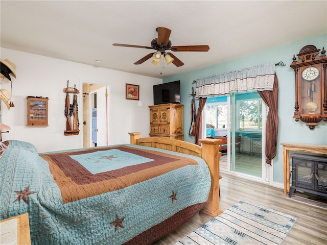 bedroom with a wood stove, ceiling fan, and hardwood / wood-style floors