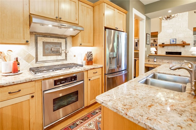 18140 Osage Trail Dr, College Station, TX 77845 - kitchen with appliances with stainless steel finishes, under cabinet range hood, a sink, light brown cabinets, and a stone fireplace