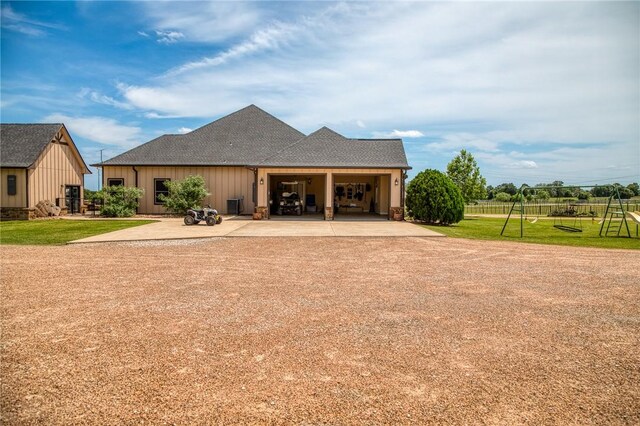 back of house with driveway, roof with shingles, board and batten siding, an attached garage, and a yard