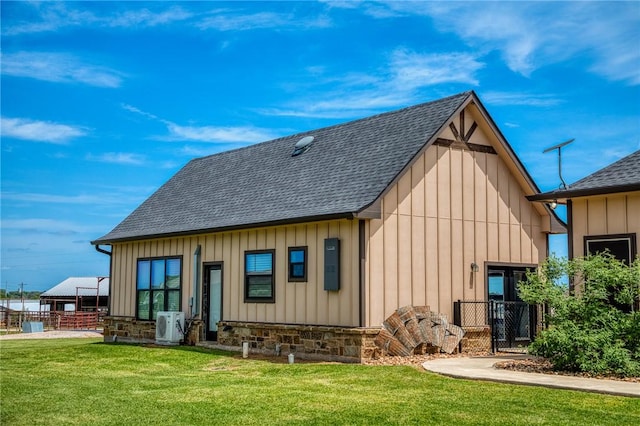 back of property with board and batten siding, ac unit, a yard, a shingled roof, and stone siding