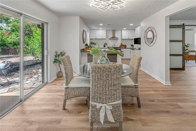 dining space with a textured ceiling, a barn door, and light hardwood / wood-style flooring