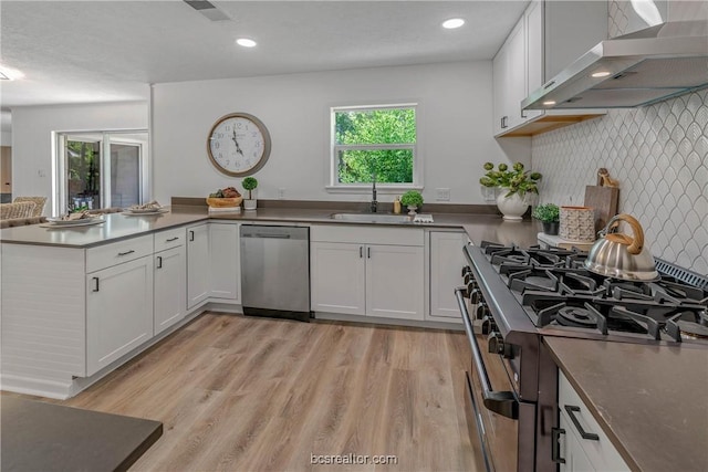 kitchen with white cabinets, a healthy amount of sunlight, wall chimney range hood, and appliances with stainless steel finishes