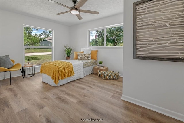 bedroom with ceiling fan, light hardwood / wood-style flooring, and multiple windows