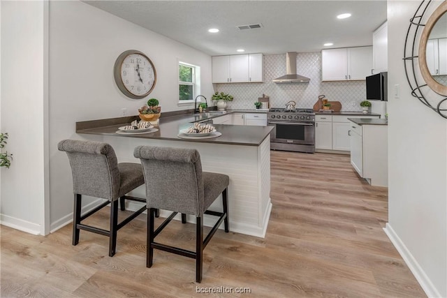 kitchen with kitchen peninsula, white cabinetry, wall chimney exhaust hood, and stainless steel range with gas stovetop