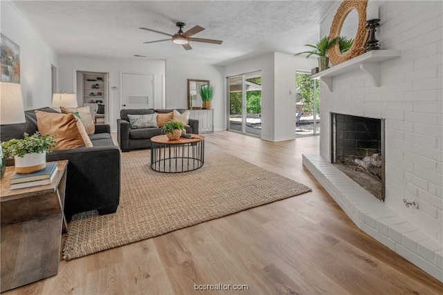 living room featuring a fireplace, a textured ceiling, light hardwood / wood-style flooring, and ceiling fan