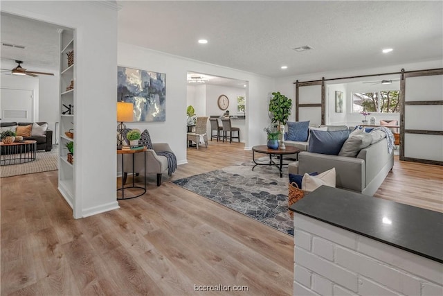 living room with a barn door, ceiling fan, light hardwood / wood-style floors, and a textured ceiling