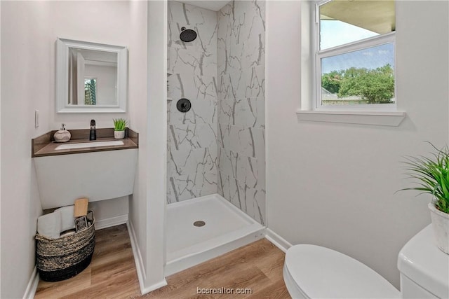 bathroom featuring wood-type flooring, a tile shower, toilet, and sink