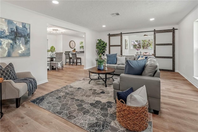 living room with crown molding, ceiling fan, a barn door, light wood-type flooring, and a textured ceiling