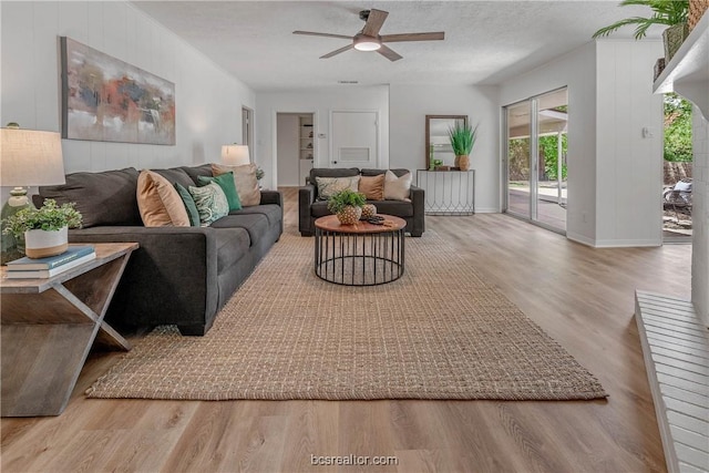 living room featuring ceiling fan, light hardwood / wood-style flooring, and a textured ceiling