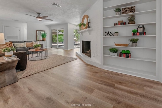 living room with a fireplace, a textured ceiling, light hardwood / wood-style floors, and ceiling fan