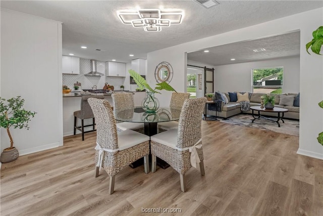 dining area with a barn door, light hardwood / wood-style floors, and a textured ceiling