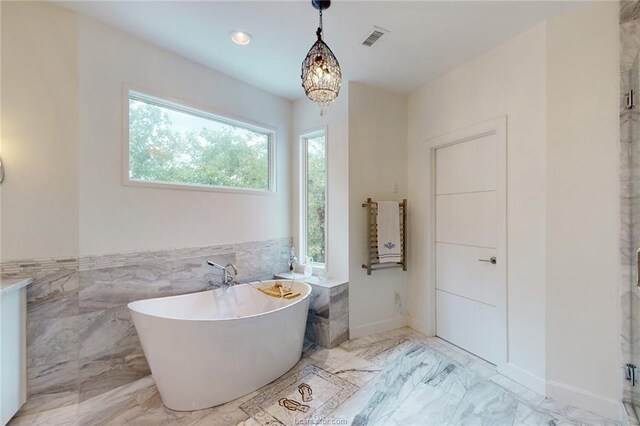 bathroom with a chandelier, a tub to relax in, and tile walls