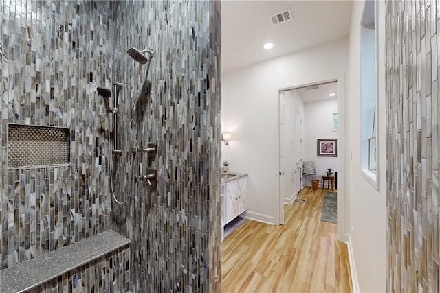 bathroom with wood-type flooring, vanity, and a tile shower