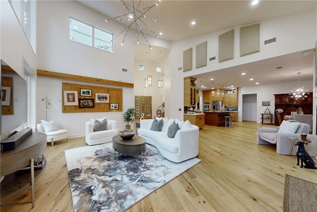 living room with light wood-type flooring, a towering ceiling, and an inviting chandelier