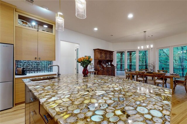 kitchen featuring stainless steel refrigerator, light hardwood / wood-style flooring, an island with sink, and sink