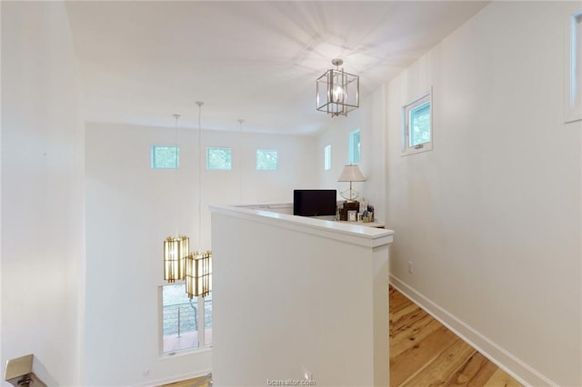 hallway featuring a healthy amount of sunlight, an inviting chandelier, and light hardwood / wood-style flooring