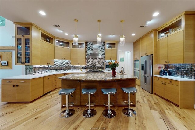 kitchen featuring appliances with stainless steel finishes, tasteful backsplash, wall chimney exhaust hood, a center island, and light hardwood / wood-style floors